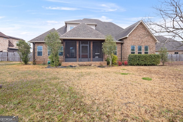 view of front of property with a front yard, a sunroom, brick siding, and fence