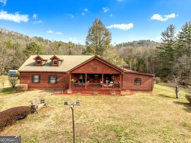 view of front of home featuring a forest view, metal roof, a porch, and a front yard