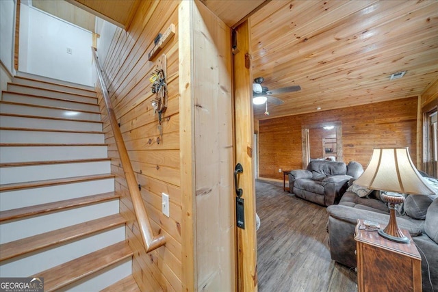 stairway with wood walls, wooden ceiling, wood finished floors, and a ceiling fan