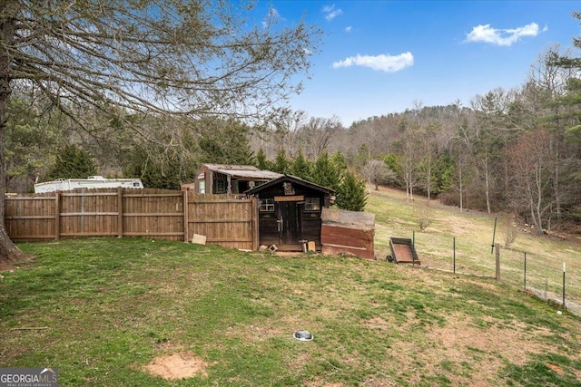 view of yard featuring fence, a wooded view, and an outbuilding