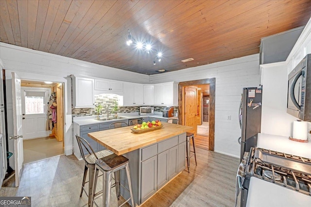 kitchen with a breakfast bar area, light wood-style flooring, stainless steel appliances, a sink, and wooden counters