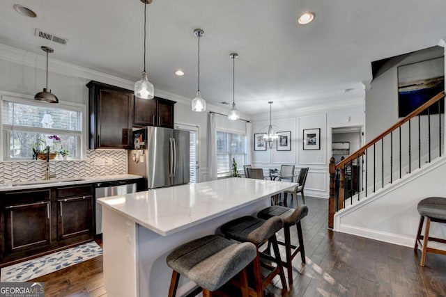 kitchen featuring stainless steel appliances, visible vents, decorative backsplash, ornamental molding, and a kitchen breakfast bar