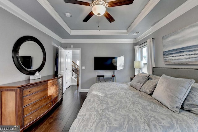 bedroom with a tray ceiling, dark wood-style flooring, visible vents, and crown molding