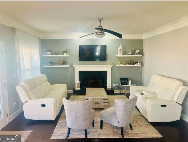 living area with dark wood-style flooring, crown molding, a fireplace, a ceiling fan, and baseboards