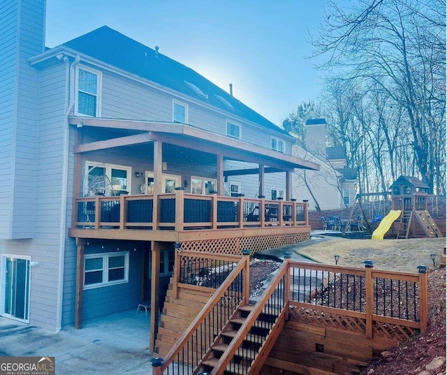 rear view of house with a playground, stairs, a yard, a wooden deck, and a chimney