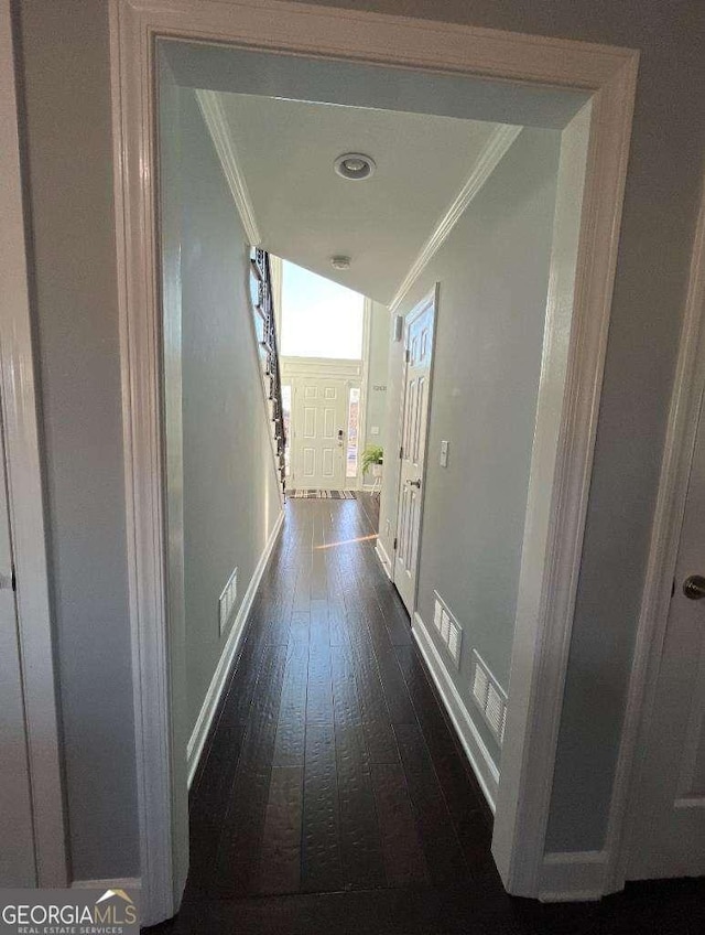 hallway featuring dark wood-style floors, ornamental molding, visible vents, and baseboards