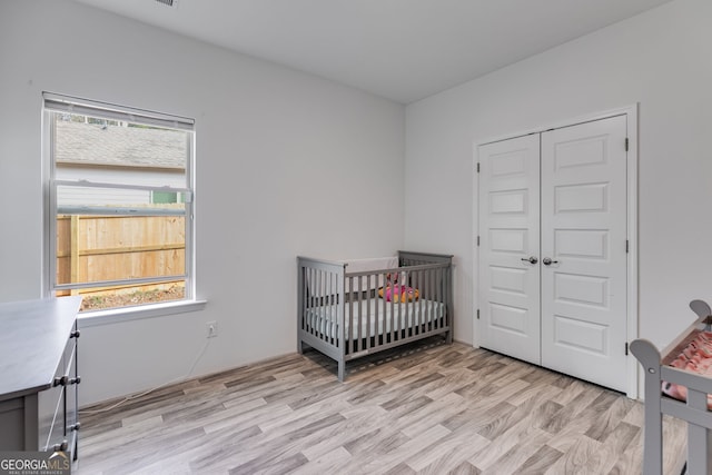 bedroom with a nursery area, light wood-style flooring, and a closet