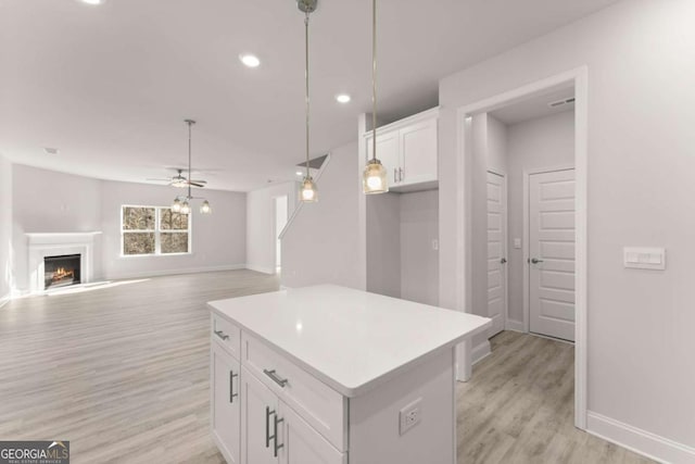 kitchen featuring a fireplace, a kitchen island, white cabinets, light countertops, and pendant lighting