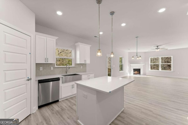 kitchen with dishwasher, a lit fireplace, light countertops, white cabinetry, and a sink