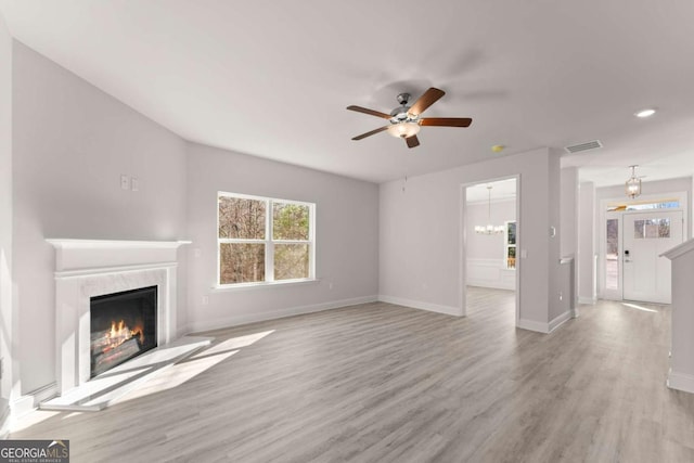 unfurnished living room featuring light wood-style floors, a fireplace, baseboards, and ceiling fan with notable chandelier