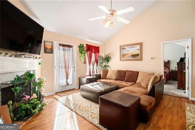 living area featuring a fireplace, a ceiling fan, wood finished floors, high vaulted ceiling, and baseboards