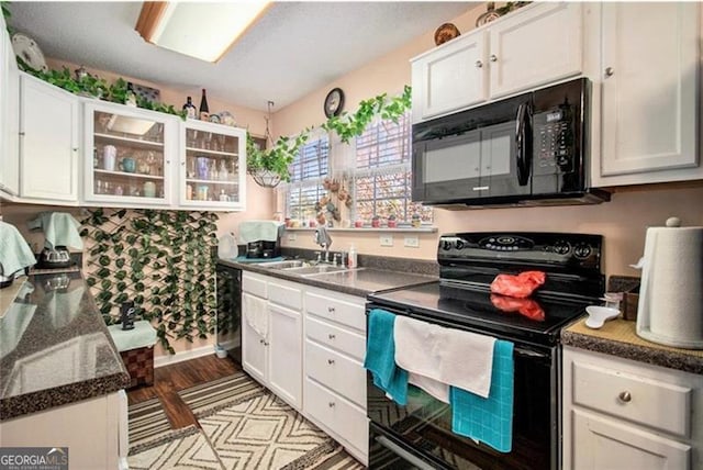 kitchen featuring dark countertops, black appliances, white cabinets, and a sink