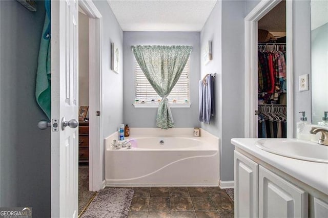 bathroom featuring a bath, a spacious closet, a textured ceiling, and vanity