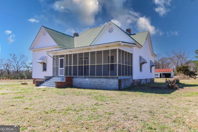 exterior space featuring a sunroom, a chimney, metal roof, and a front yard