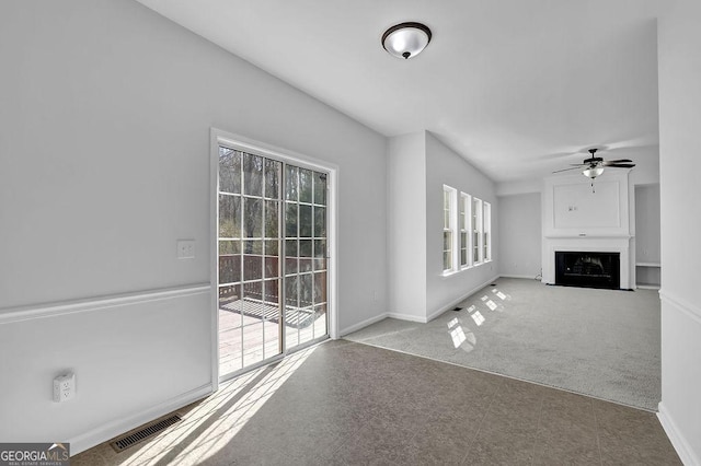 unfurnished living room featuring visible vents, baseboards, a fireplace with flush hearth, ceiling fan, and carpet