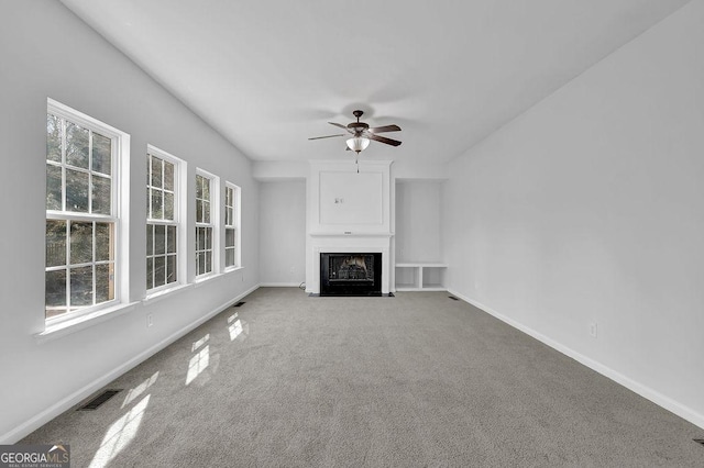 unfurnished living room with a fireplace, visible vents, carpet flooring, ceiling fan, and baseboards