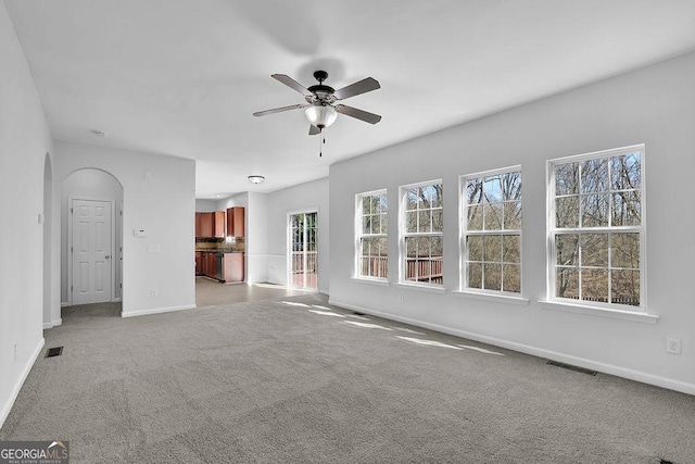 unfurnished living room featuring arched walkways, ceiling fan, visible vents, baseboards, and carpet