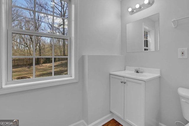 half bath with plenty of natural light, vanity, toilet, and baseboards