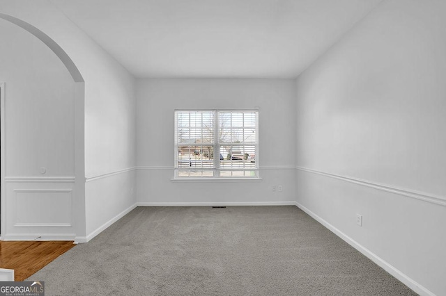 carpeted spare room with arched walkways and baseboards