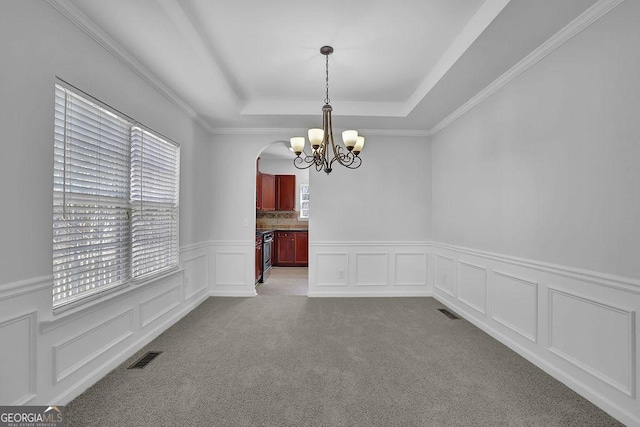 unfurnished dining area with a tray ceiling, carpet flooring, visible vents, and a decorative wall