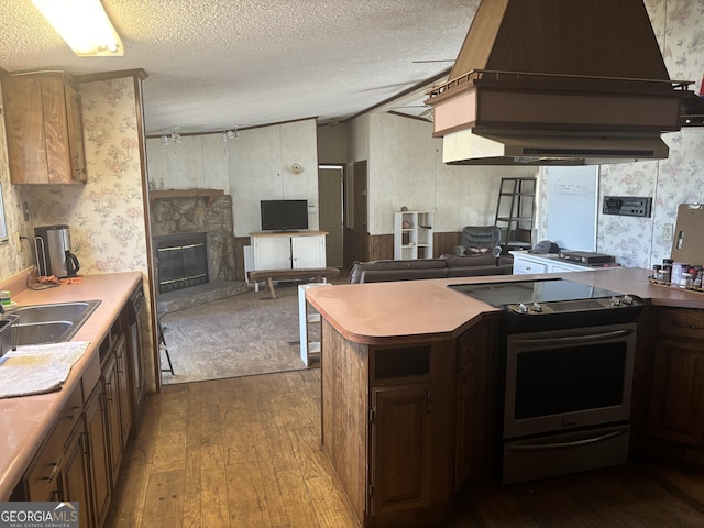 kitchen featuring wallpapered walls, dark wood-style flooring, a textured ceiling, stainless steel range with electric cooktop, and a fireplace