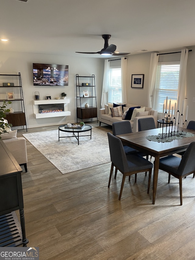 dining area with wood finished floors, a glass covered fireplace, and a ceiling fan