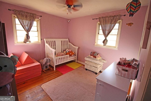 bedroom featuring ceiling fan, a crib, and wood finished floors