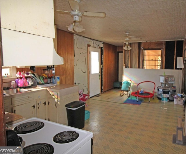 kitchen with ceiling fan, white electric range, wood walls, and a sink