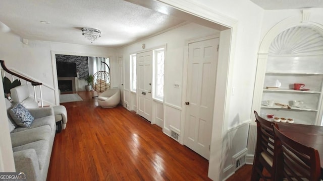 entrance foyer with a textured ceiling, a fireplace, wood finished floors, and visible vents