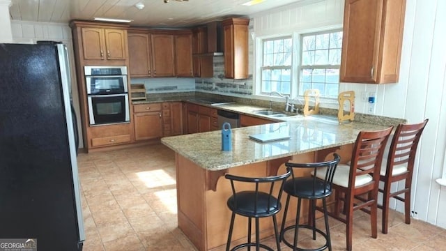 8875 E Broad St, Sparta, GA 31087 - kitchen with a peninsula, wall chimney exhaust hood, stainless steel appliances, a sink, and brown cabinetry