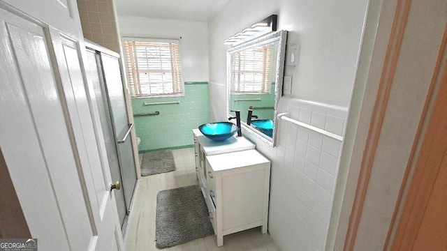 full bathroom featuring a wainscoted wall, wood finished floors, vanity, tile walls, and a shower stall