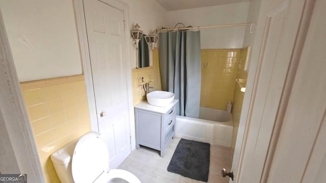 bathroom featuring toilet, vanity, shower / bath combo with shower curtain, and tile walls