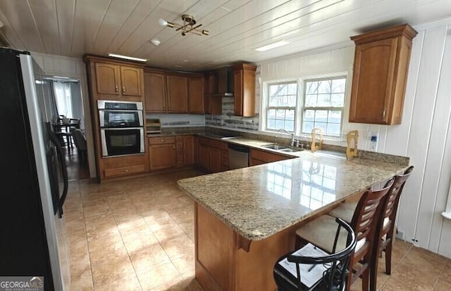 kitchen with wooden ceiling, wall chimney exhaust hood, brown cabinets, a peninsula, and stainless steel appliances