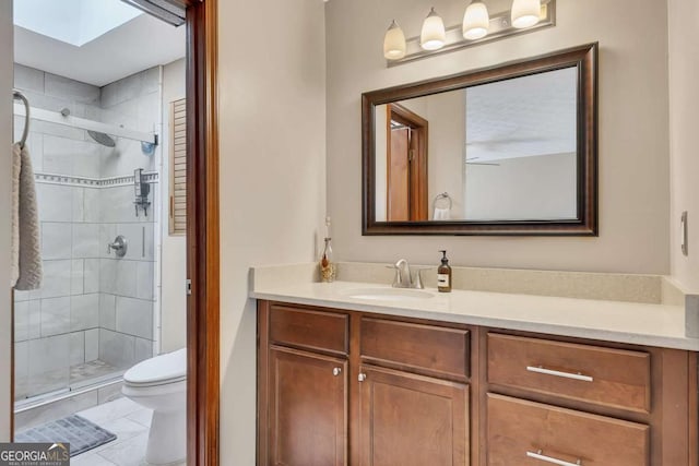 bathroom featuring a skylight, toilet, a shower stall, vanity, and tile patterned floors