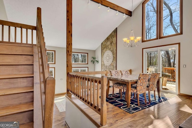 dining space featuring a notable chandelier, rail lighting, wood finished floors, high vaulted ceiling, and baseboards