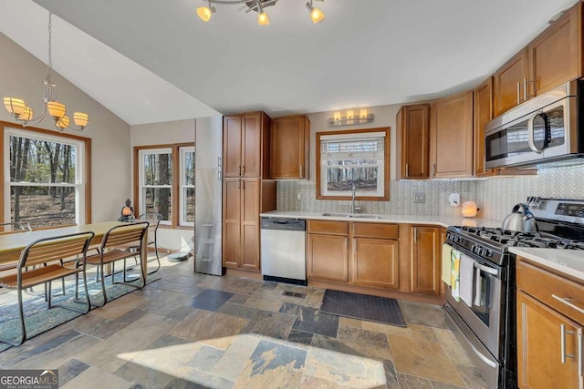 kitchen with stainless steel appliances, a sink, stone tile flooring, and brown cabinets