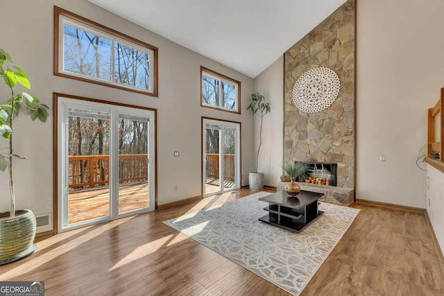 living area with high vaulted ceiling, a fireplace, wood finished floors, and baseboards