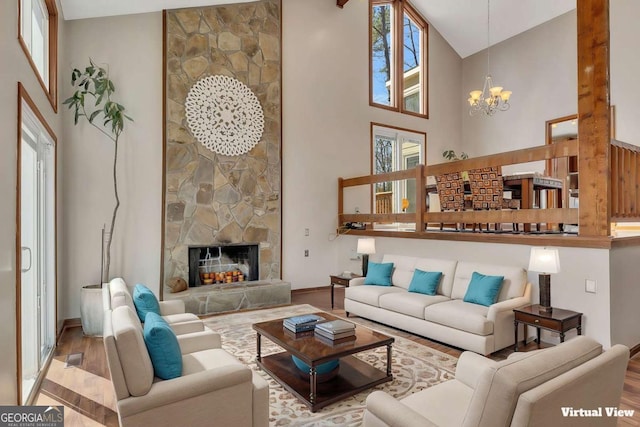 living area with a stone fireplace, wood finished floors, a towering ceiling, and a notable chandelier