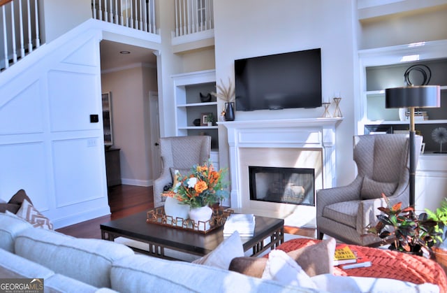 living area featuring built in shelves, a high end fireplace, baseboards, and wood finished floors