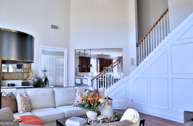 living area with a decorative wall, dark wood-type flooring, a towering ceiling, visible vents, and stairway