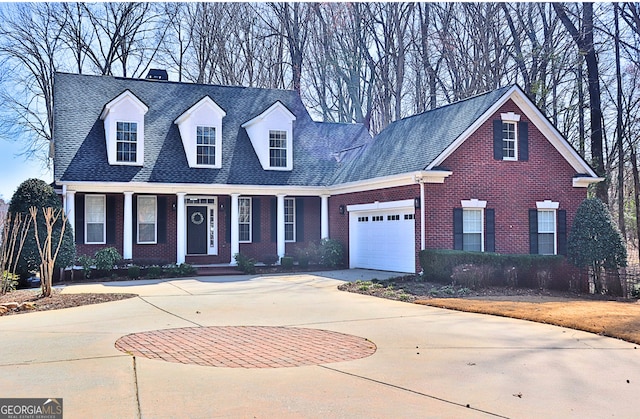 cape cod home with a garage, brick siding, concrete driveway, roof with shingles, and a chimney