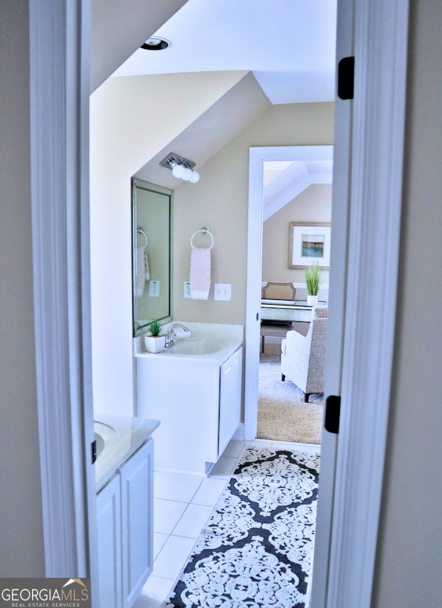 bathroom with lofted ceiling, a sink, two vanities, and tile patterned floors