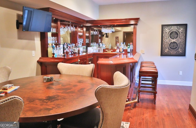 bar with a bar, wood finished floors, and baseboards