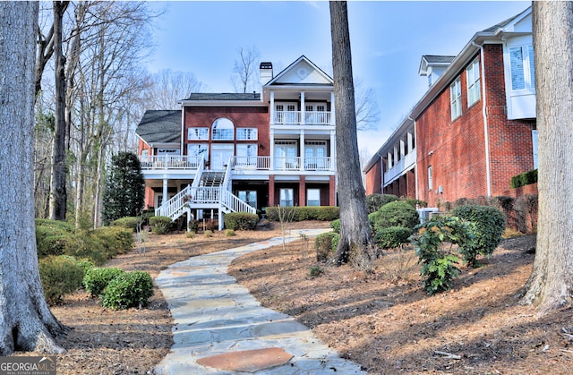 rear view of property featuring a balcony, stairs, a chimney, and brick siding