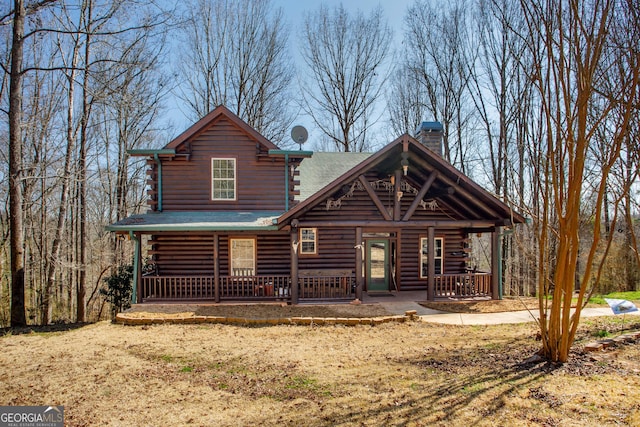 cabin with a porch, a chimney, and log exterior