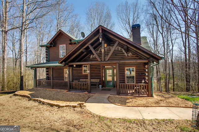 log home featuring covered porch, a chimney, and log exterior