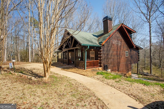 exterior space featuring a chimney, covered porch, roof with shingles, and log exterior