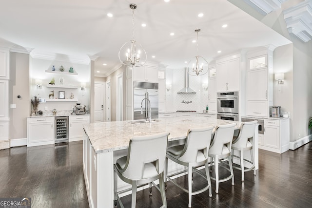 kitchen featuring wine cooler, appliances with stainless steel finishes, white cabinetry, a sink, and wall chimney range hood