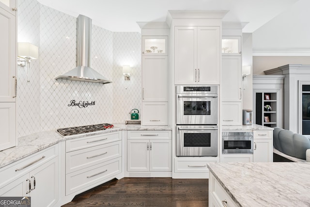 kitchen with white cabinets, wall chimney exhaust hood, glass insert cabinets, and stainless steel appliances