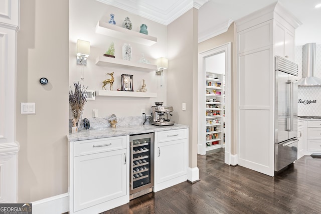 bar with wine cooler, ornamental molding, stainless steel built in fridge, a bar, and wall chimney exhaust hood